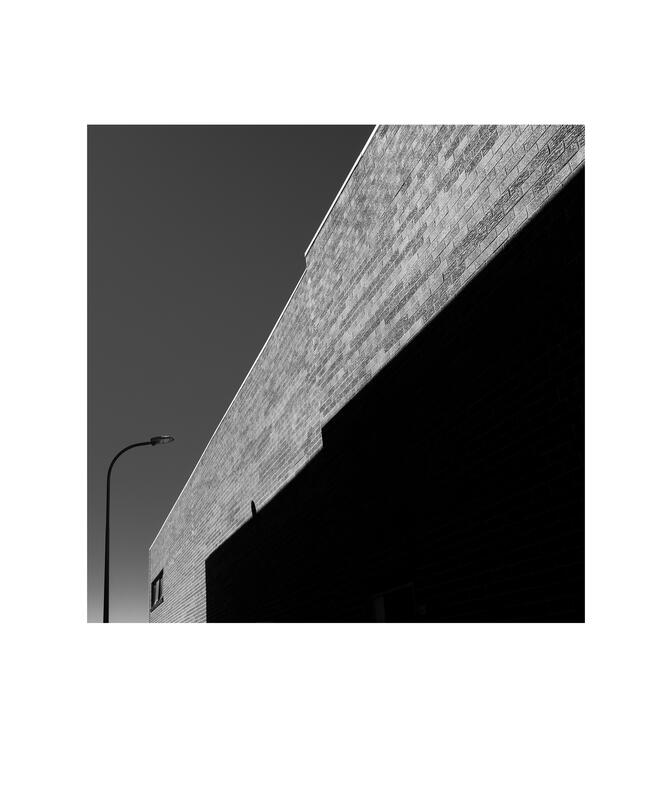 Black and white photograph by Bradley Cummings titled BRICK WALL WITH SHADOW AND STREET LIGHT Canberra, 2026.
